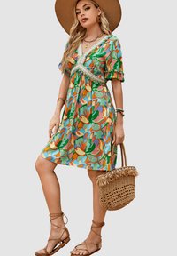 Vestido floral en vibrantes patrones verdes, naranjas y azules; mangas cortas con volantes; borde de encaje en el escote; combinado con un bolso de paja.