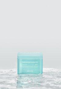 Contenant des tampons Turquoise Mediheal Madecassoside Blemish sur une surface humide avec reflet d'eau, fond gris neutre.