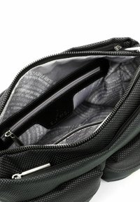 Czarna torebka z teksturowanej tkaniny wewnątrz z wieloma przegródkami i zamkami, z szarym podszewką w powtarzającym się wzorze logo.