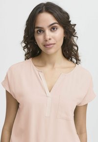 Blusa rosa chiaro a maniche corte con scollatura a V e tasca, realizzata in tessuto liscio con dettagli di cucitura sottili.
