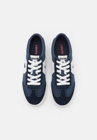 Zapatillas de color azul marino con detalles en blanco, confeccionadas en ante y lona, presentan un diseño clásico de cordones, costuras en contraste y un logotipo en la lengüeta.