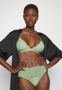 Bralette verde claro de renda com padrão floral, combinado com roupa interior de cintura alta a condizer. Robe preto de cetim com detalhes em renda.