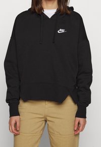 Zwarte hoodie van zachte stof, met een kangoeroetas, verlaagde schouders en een wit Nike-logo op de borst.