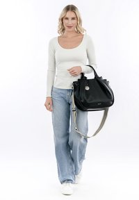 Black leather handbag with a structured shape, short handles, and a detachable shoulder strap. Model wears a fitted white long-sleeve top and light blue jeans.