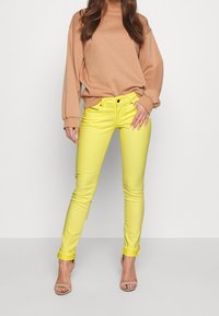Gula jeans i skinny-modell med slim fit, stylade med en beige oversized sweatshirt. Jeansen har en uppvikt fåll och framfickor.