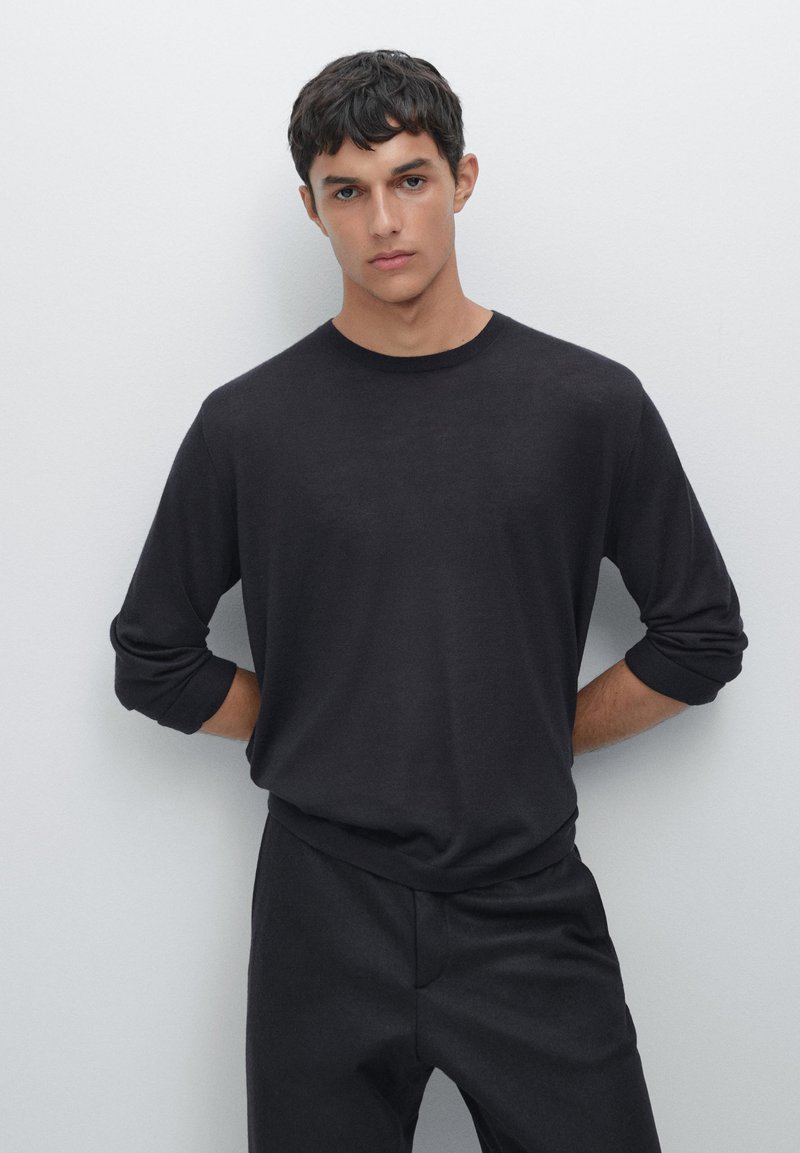 Czarna, długosleeve'owa koszula z miękkiego materiału, z okrągłym dekoltem i lekko podwiniętymi rękawami, w połączeniu z ciemnymi spodniami.