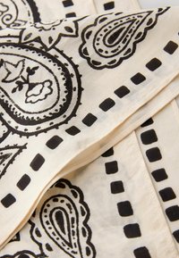 Beiger Stoff mit schwarzen Paisley- und gepunkteten Randmustern, übereinander gefaltet.