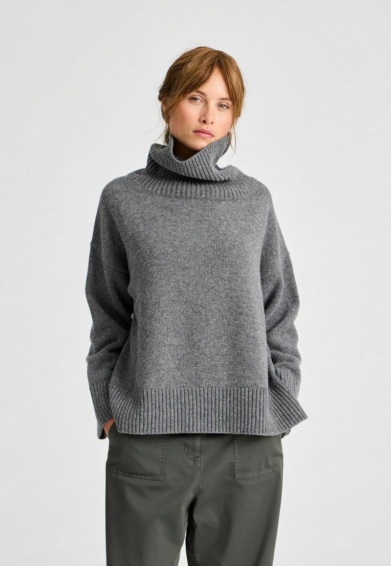 Maglione a collo alto grigio a maglia con colletto e orlo a coste. Vestibilità ampia e maniche lunghe. Abbinato a pantaloni verde oliva.