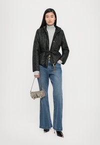 Black quilted jacket with a tied waist, gray turtleneck, wide-leg blue jeans, black pointed heels, and a metallic handbag.
