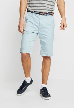 Jasnoniebieskie szorty o gładkiej fakturze, z wywijanymi mankietami i bocznymi kieszeniami, w połączeniu z wzorzystym paskiem i granatowymi sneakersami.