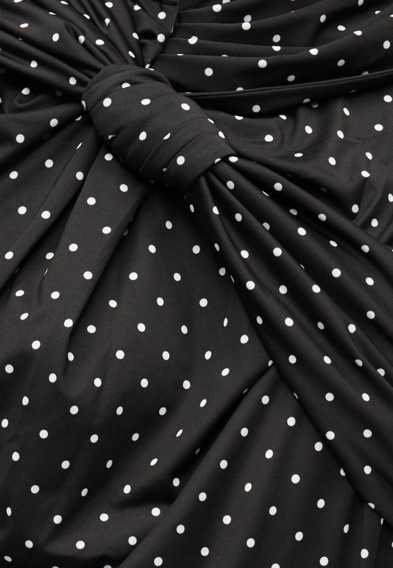 Tissu noir à pois blancs, présentant un design noué et une texture froncée pour plus de dimension et d'intérêt visuel.