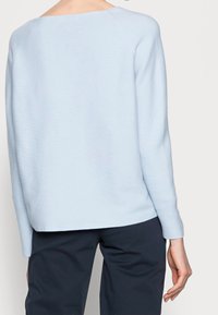 Pull tricot bleu clair avec dos dégagé, manches longues et coupe ample, associé à un pantalon bleu marine. Texture douce avec des détails côtelés.