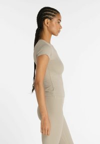 Top aderente a maniche corte in leggero tessuto a coste beige chiaro; texture liscia e collo girocollo classico con dettagli di cucitura sottili.