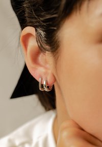Des boucles d'oreilles créoles en argent présentent une surface lisse et polie avec un design courbé et élégant. Elles se portent à l'oreille, soulignant la forme de celle-ci.