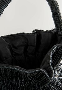 Melna pērlīšu soma ar strukturētu virsmu, kurai ir mīksta auduma oderējums. Atvērta augšdaļa un austs rokturis ērtai nēsāšanai.