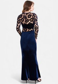Lungo abito in velluto blu navy con corpetto in pizzo floreale ricamato a maniche lunghe, vita aderente e gonna svasata. Texture liscia e morbida in tutto il capo.
