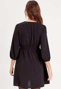 Robe noire présentant une coupe décontractée avec une taille élastique, des manches ballon trois-quarts, et un tissu léger et lisse.
