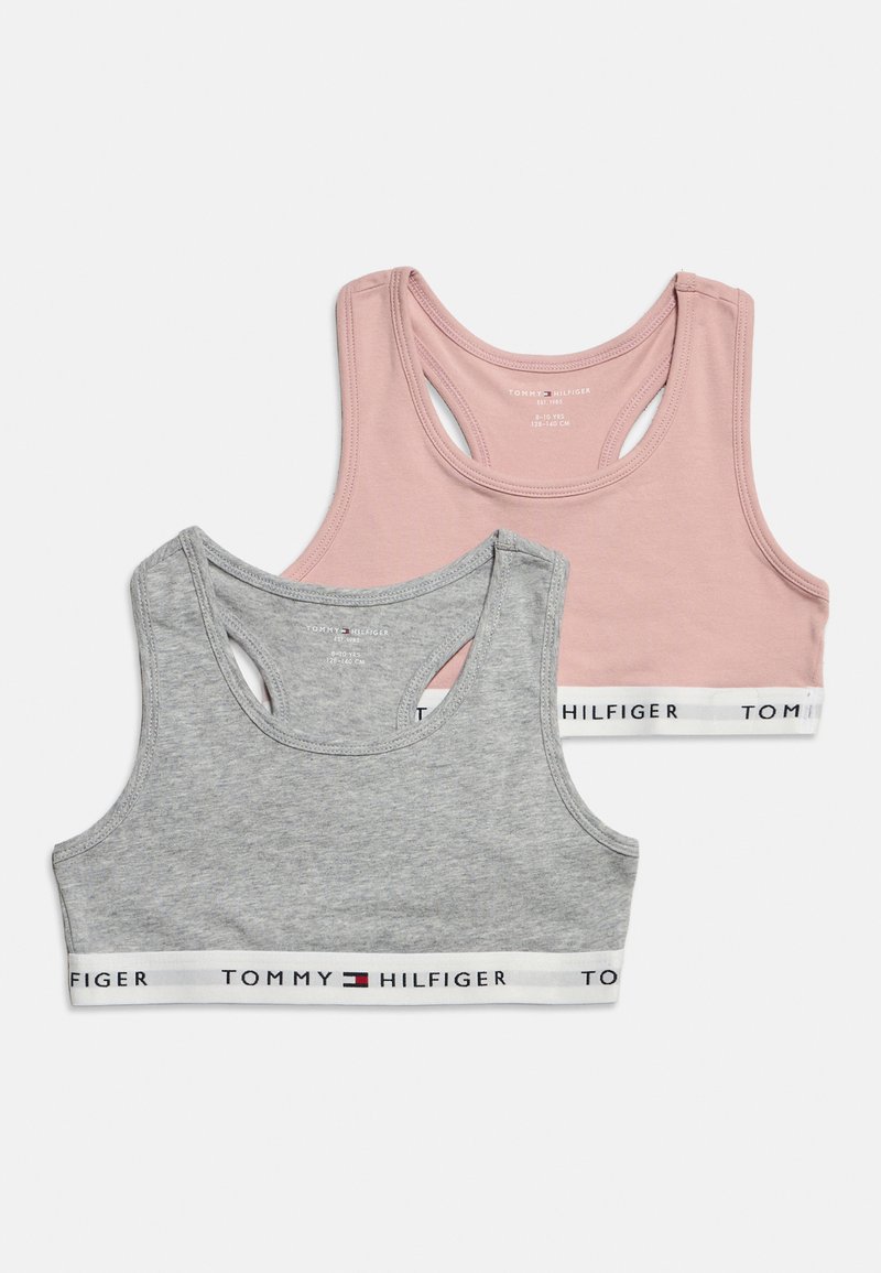 Δύο αθλητικά σουτιέν Tommy Hilfiger, ένα ροζ και ένα γκρι, με ελαστικές ταινίες με λογότυπο, τοποθετημένα πάνω σε λευκό φόντο.
