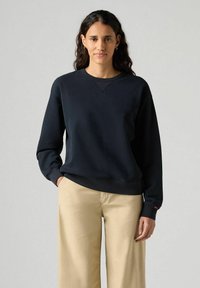 Sudadera azul marino hecha de un tejido suave y texturizado. Presenta un cuello redondo, puños y dobladillo acanalados, con un pequeño detalle de logo en la manga.