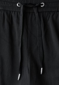 Black shorts with an elastic waistband, featuring a drawstring closure, black fabric, and silver hardware accents. Smooth texture.