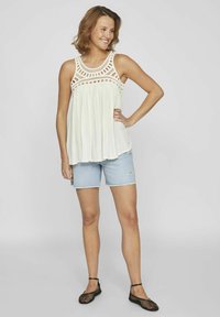Top blanco sin mangas con detalles de crochet en el escote, combinado con pantalones cortos de mezclilla azul claro y zapatos negros de malla tipo slip-on.