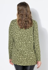 Maglia verde a maniche lunghe con motivo a stampa leopardata, caratterizzata da una vestibilità comoda e tessuto morbido, indossata con leggings neri.