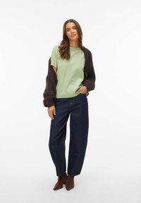 Jasnozielony t-shirt z krótkim rękawem, oversize'owy ciemnobrązowy sweter na drutach, ciemnoniebieskie dżinsy z wysokim stanem oraz brązowe botki na obcasie.