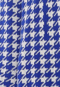 Tessuto blu con un motivo a scacchi bianco, dall'aspetto di maglia testurizzata, creando un forte contrasto visivo.