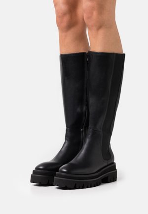 Black leather knee-high boots with a chunky rubber sole, featuring side zippers and elastic panels for ease of wear.