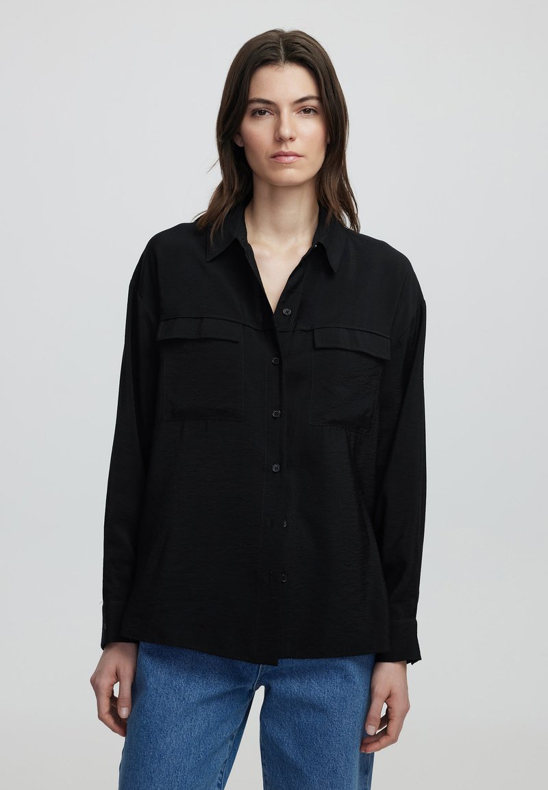 Camicia nera a maniche lunghe con bottoni, due tasche sul petto e una vestibilità comoda. Realizzata in tessuto testurizzato, presenta un colletto e polsini a punta.