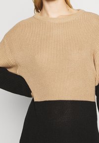 Stickad tröja i blockdesign med en beige övre del och en svart nedre del. Rundad halsringning och lös passform med strukturerad tyg.