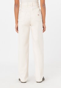 Pantalones de pierna ancha en color crema, fabricados con un tejido duradero, que cuentan con una cintura alta, dos bolsillos traseros y un logo de la marca en el bolsillo derecho.