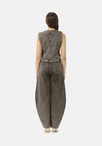 Mono de mezclilla gris con un diseño sin mangas, corsé ajustado, pantalones de pierna ancha y cremallera en la parte posterior. Incluye bolsillos traseros y detalles de costura.