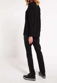 Top a maniche lunghe nera abbinato a pantaloni neri con una striscia bianca. L'outfit ha una vestibilità comoda, con tessuto morbido e design minimalista.