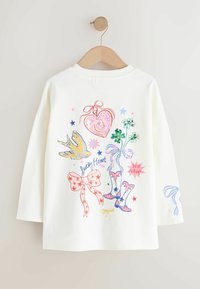 Biała bluza z kolorowymi grafikami, w tym sercem, ptakiem, koniczynkami i kokardkami. Projekt zawiera gwiazdy i wesołe akcenty.