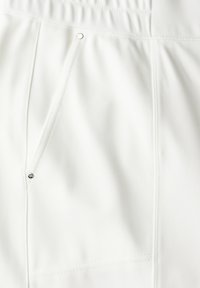 Vitt tyg med en diagonal struktur, med en sidficka med tryckknapp och prydliga sömmar genom hela.