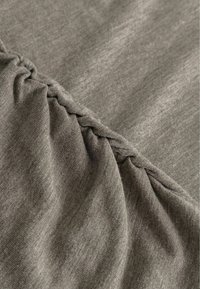 Pelēks audums, kas ir drapēts ar savilktu detaļu gar vienu malu, ar gludu tekstūru un nemanāmiem toņu variantiem.