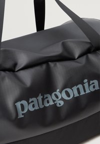 Czarna torba typu duffle wykonana z gładkiego, wytrzymałego materiału. Posiada wyraźne logo "patagonia" w jasnoniebieskim kolorze. Paski są wzmocnione.