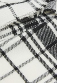 Tessuto a scacchi bianco e nero, caratterizzato da una consistenza morbida con bordi sfrangiati, disposto in strati sovrapposti.