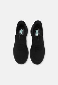 Paire de chaussures Skechers noires sans lacets avec dessus en tissu tricoté et semelles intérieures rembourrées, vues de dessus sur un fond uni.