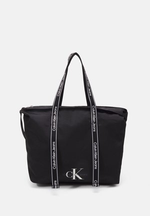 Czarna torba typu tote z białym logo Calvin Klein Jeans i czarnymi uchwytami z nadrukowaną nazwą marki.