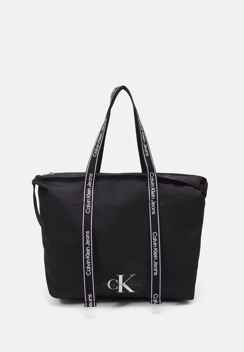 Sac cabas noir avec logo Calvin Klein Jeans blanc et poignées noires imprimées du nom de la marque.