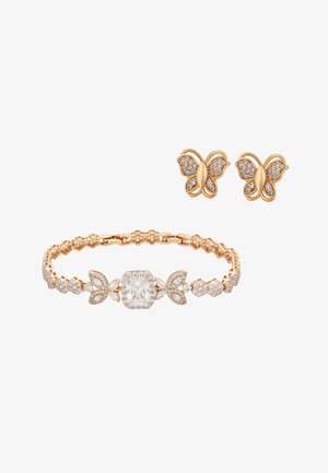 Gouden oorknopjes in de vorm van een vlinder met heldere kristalaccenten, gecombineerd met een gouden armband met een groot centraal kristal en vlindermotieven.