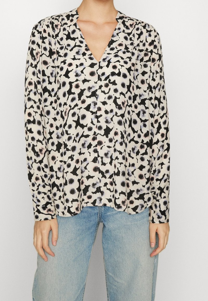 Langarmbluse in Creme mit schwarzem und pastellfarbenem Leopardenmuster, V-Ausschnitt, aus weichem Stoff und entspannter Passform. Kombiniert mit blauen Jeans.