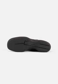 Fekete sneaker, textúrált talppal, mély barázda mintázattal és enyhén megemelt sarkával. Egyszerű dizájn, minimális kiegészítőkkel.