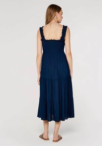 Marineblaues, gestuftes Maxikleid mit Rüschenträgern und gerafftem Oberteil. Hergestellt aus leichtem Stoff, bietet es eine luftige Silhouette und pastellfarbene Akzente.