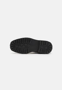 Suola di scarpa in gomma nera con scanalature profonde e prominenti, progettata per una maggiore aderenza e durata. Presenta un lato inferiore texturizzato.