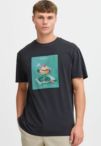Sort bomulds T-shirt med et farverigt trykt design af en dessert på en glasplatte, med tekst ovenfor og nedenfor billedet. Korte ærmer.