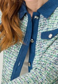 Kurtka z denimu i tkaniny o fakturze z niebieskim kołnierzem, srebrnymi guzikami oraz wzorem w kilku kolorach: zielonym, białym i niebieskim.