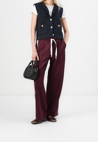 Tmavě modrá pletená vesta se zlatými knoflíky, pod ní bílý tričko, široké vínově červené kalhoty se bílým šňůrkovým páskem, černá kabelka, boty s leopardím vzorem.